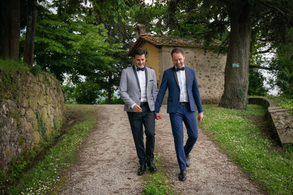 two grooms walking hand by hand on a country road